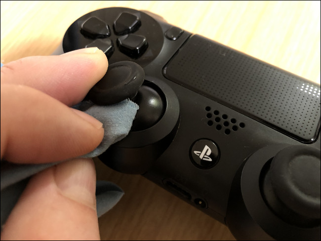 A hand cleaning an analog stick with a cloth on a DualShock 4 Controller.