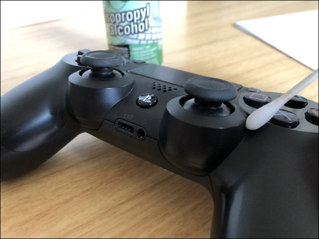 A DualShock 4 Controller with a Q-tip on top of it next to a bottle of isopropyl alcohol.