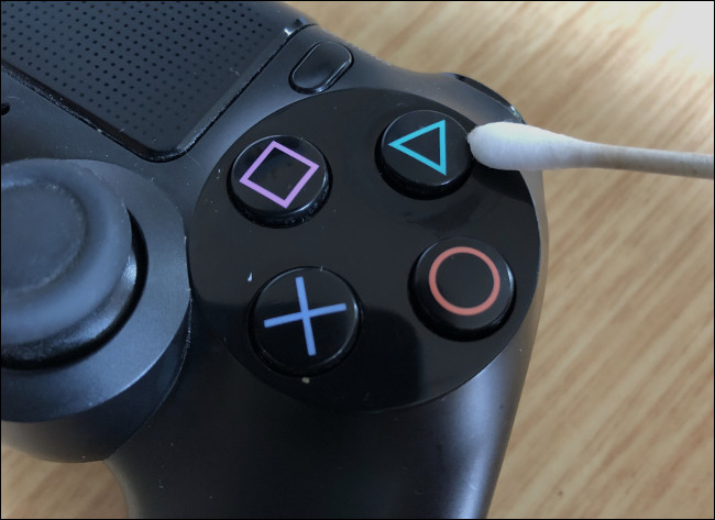 A Q-tip wiping a button on a DualShock 4 Controller. 