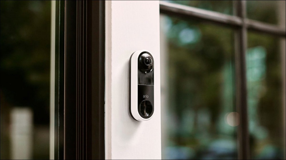 An Arlo doorbell installed beside a glass front door.